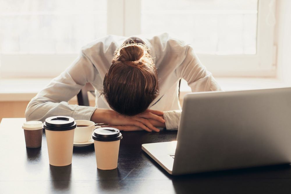 Woman with her head down on her desk and several coffee cups